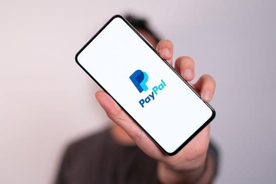 A man holding a phone with the PayPal logo visible on the phone screen.
