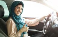 Happy Arab woman in hijab driving her car with a thumbs-up.