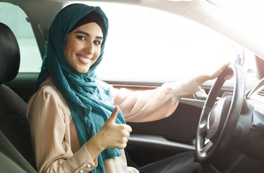 Happy Arab woman in hijab driving her car with a thumbs-up.
