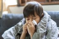 Young Asian boy sneezing and having a runny nose.
