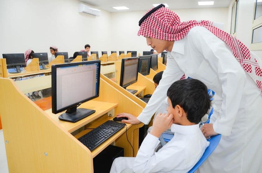 In a Computer Education Laboratory, a teacher instructs students on using computers.