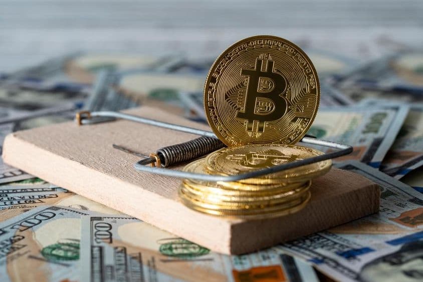 Gold cryptocurrency coins bitcoin in a mousetrap, with US 100 dollar bills in the background.