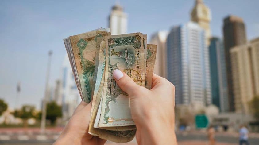 A girl holding UAE currency with Dubai skyscrapers in the background.