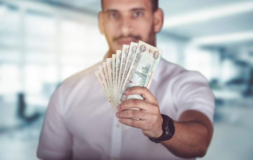Man holding dirham banknotes, standing in front of a bank branch.