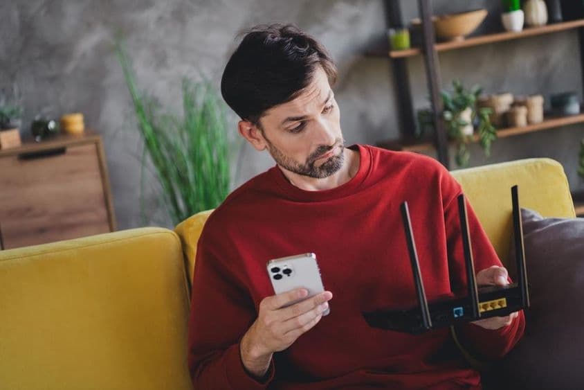 A young man relaxing at home with a smartphone and router, enjoying a peaceful afternoon.