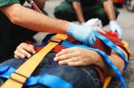 Emergency service personnel assist an injured individual on a stretcher.