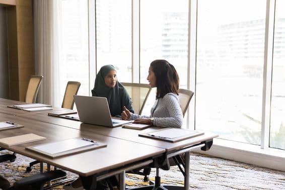 Two colleagues sitting at a large desk in an office, chatting.