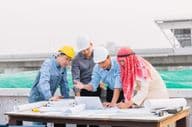 Arab businessman, engineer, and worker engage with construction plans using a laptop.