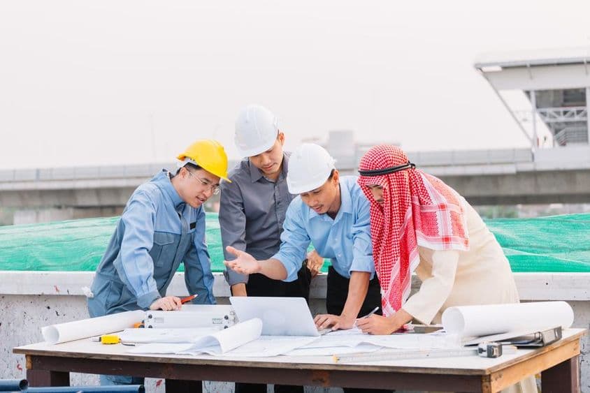 Arab businessman, engineer, and worker engage with construction plans using a laptop.