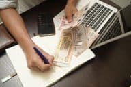 A man sitting at a desk counting a stack of UAE dirham banknotes.