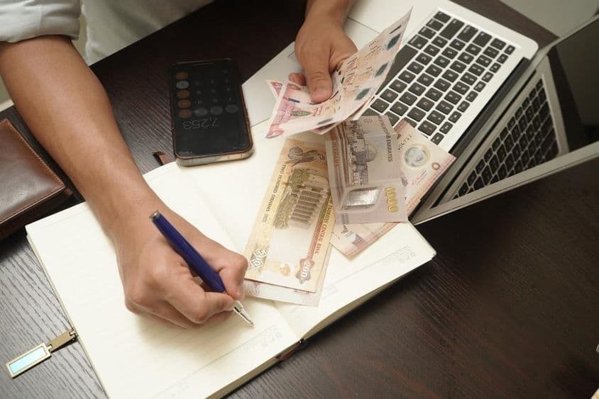 A man sitting at a desk counting a stack of UAE dirham banknotes.