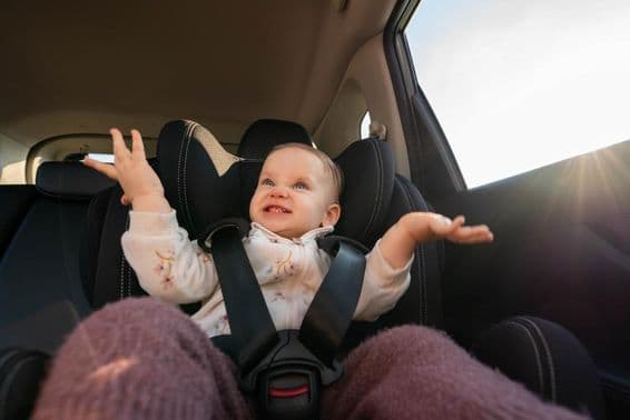 Happy baby clapping in a car seat during a family trip.