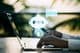 A person typing on a laptop with a blurred outdoor background featuring a chatbot icon.
