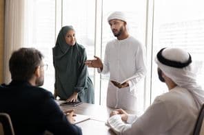 A group of young Arab managers in traditional Muslim attire presenting a project to European business partners.