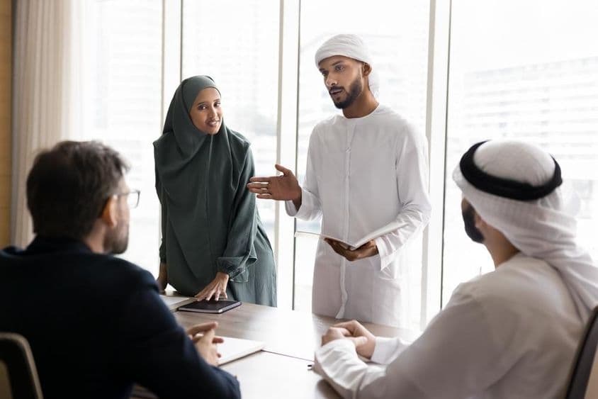 A group of young Arab managers in traditional Muslim attire presenting a project to European business partners.
