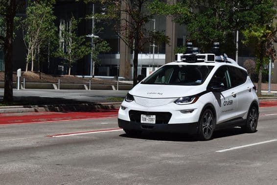 A white, supervised autonomous car cruising in the downtown financial district.