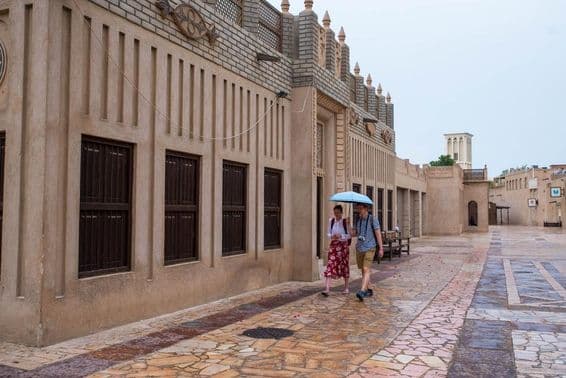 A tourist couple walking under an umbrella on the streets of Dubai.