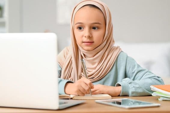 Little Muslim girl in hijab doing homework at home.