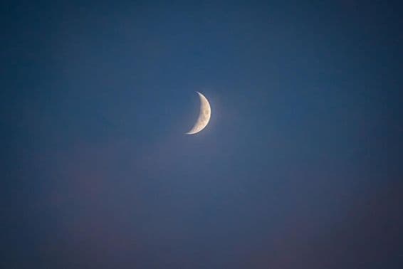Crescent moon at dusk with whispering clouds.