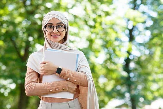 Back to school, Arab woman in hijab and glasses holding books in park.