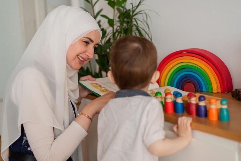 A Muslim teacher and a kindergarten-aged child play with colorful toys.