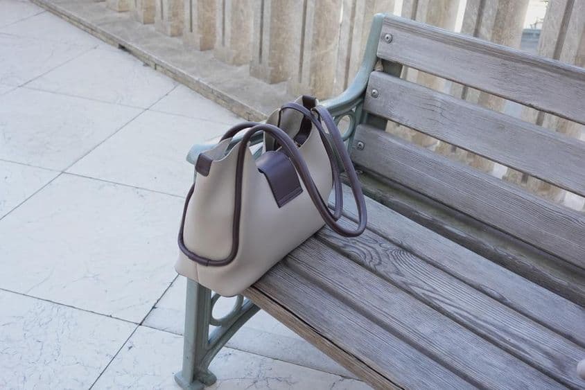 Bag resting on a wooden bench in an urban setting.