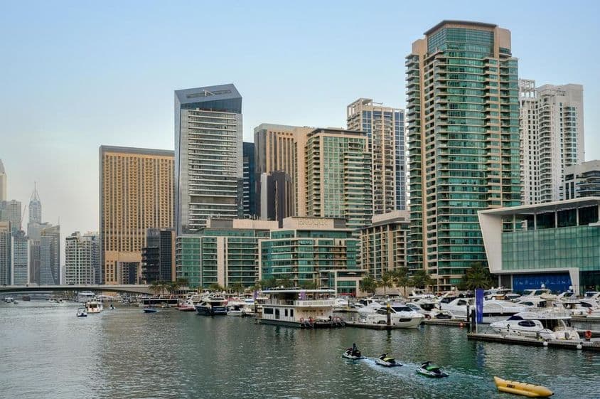 Evening view of the canal, harbor with boats, Dubai promenade, and skyscrapers.