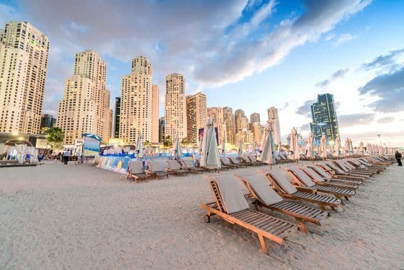 Sunset at Marina Beach, Dubai, with beach chairs and skyscrapers.