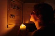 Young woman examines fuse box at home in complete darkness with candles.