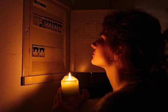 Young woman examines fuse box at home in complete darkness with candles.