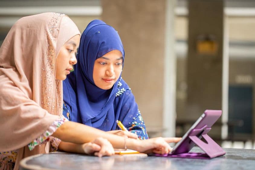 Two Muslim students working on a tablet.