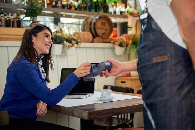 Brown-haired woman seated in a café, paying with a credit card.