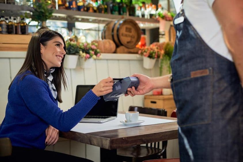 Brown-haired woman seated in a café, paying with a credit card.