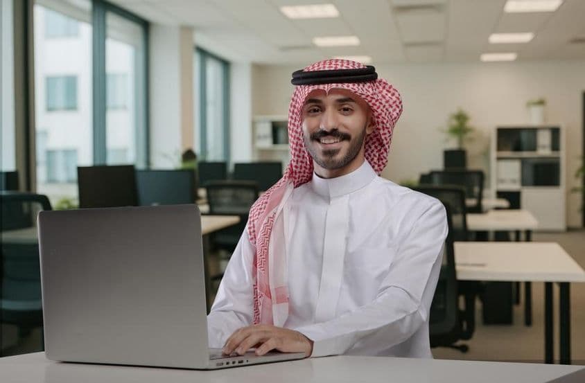 Smiling Saudi Arabian man in traditional attire working.