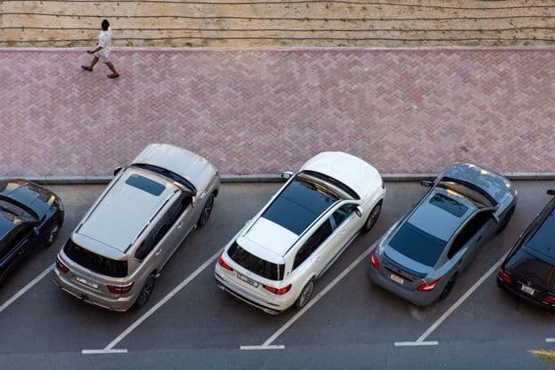 Overhead view of parked cars in Dubai and a man walking on a paved sidewalk.