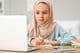 Little Muslim girl doing homework at home wearing hijab.