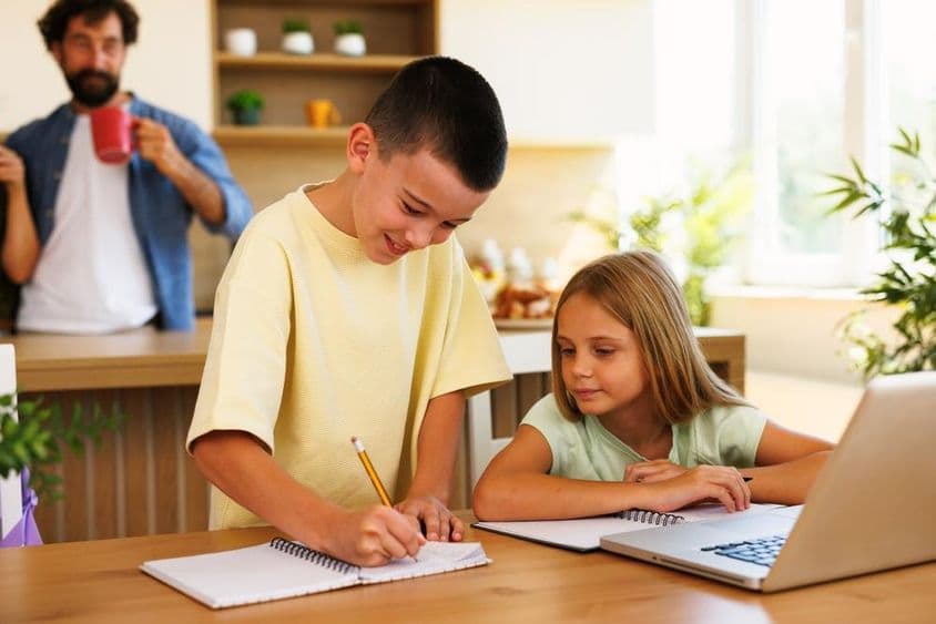 Siblings doing homework at home using laptop.