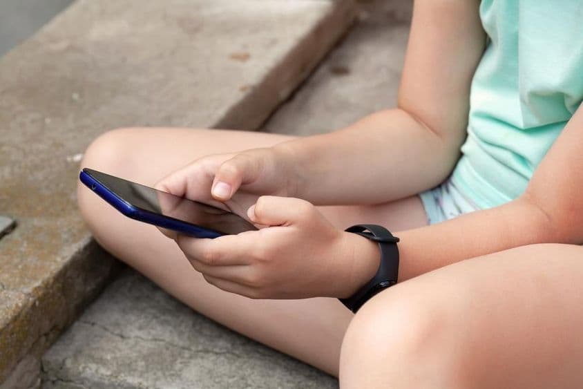 A child sits outdoors using a smartphone.