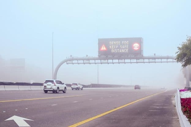Foggy road with a sign mentioning Keep Distance.