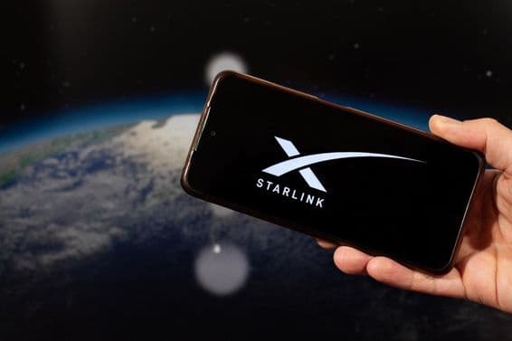 A male hand holding a smartphone with the Starlink logo in his right hand.