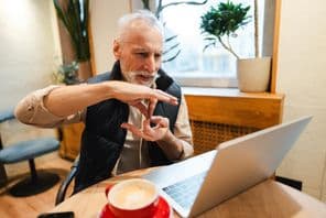 An older bearded man speaking sign language during a video call.