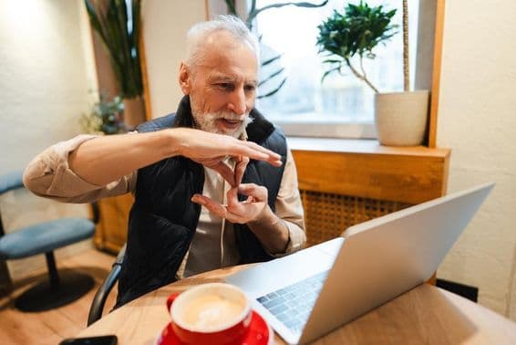 An older bearded man speaking sign language during a video call.