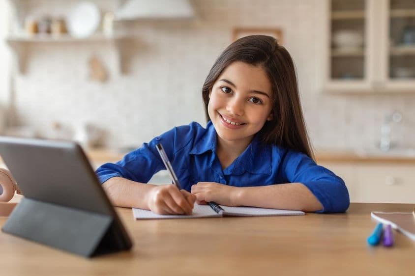 Happy schoolgirl attending classes from home using a tablet.