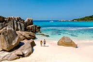 Two travelers walking on the soft white sands of Anse Cocos Beach in Seychelles.