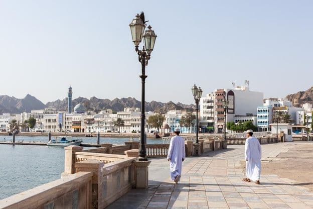 Men in traditional Omani attire along Muscat waterfront.