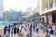 A diverse crowd of tourists and locals walks along the busy waterfront promenade in front of Dubai Mall.